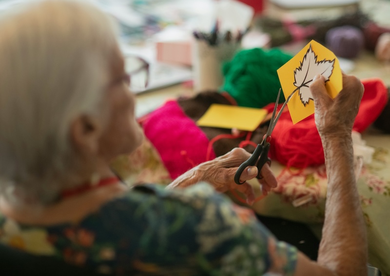 elderly woman sat down cutting out a leaf on paper